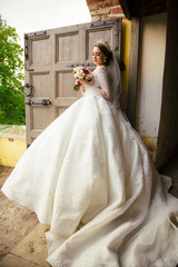 Fototapeta premium Beautiful Bride in a white Wedding Dress outdoors with a Bouquet of flowers and a veil