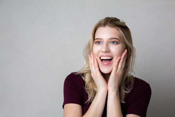 Excited blonde woman with natural makeup posing against grey background. Space for text