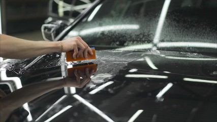 professional applying protective film to the red car. Master glues a protective film on the hood of...