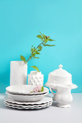 Mock up image with white Crockery,dish, utensils and flower vases on grey table against blue background with space for design. Kitchen still life as background for design. Copy space.