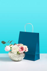 Mock up image with rose flowers in vase near paper gift bag stand on blue background. Gift concept image with space for design. Flower shop. Branding mock up. Concept for sales or discounts