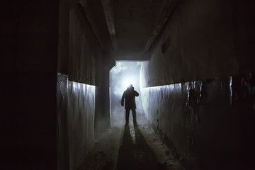 Silhouette of man in standing in dark scary corridor or tunnel with back light