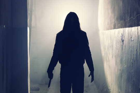 Silhouette of criminal or maniac or rapist with knife in hand and long hair in old scary corridor, man killer with cold weapon, halloween and thriller movie atmosphere