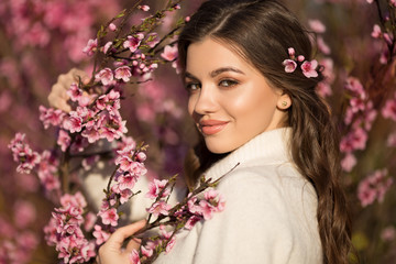 Pretty smiling teen girl posing near blossom cherry tree with pink flowers.