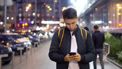 Young Attractive Man Using Smartphone in the evening city street with bokeh light effect.