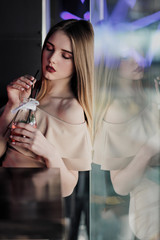 Young beautiful brown-haired girl in a nightclub with neon lights sits by the glass and drinks a red cocktail.