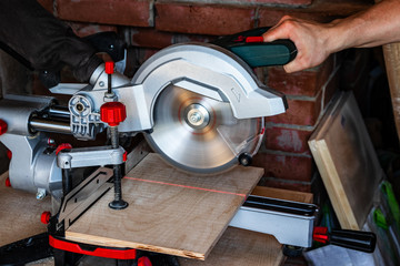 Works miter saw. The red line of the laser target pointer in the place of the future cut. The hand of a carpenter man controls the saw.