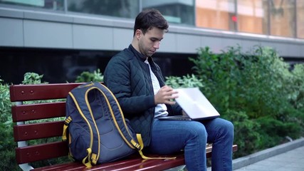 Young attractive student finished working on laptop in the street and go out.