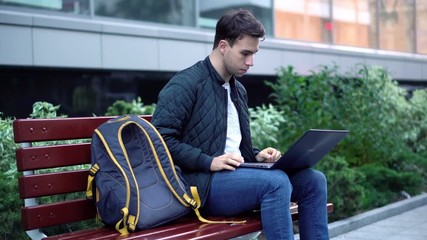 Young attractive student working on laptop in the street 