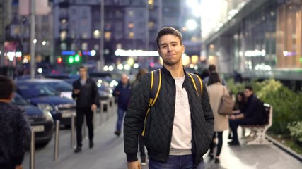 Young happy smiling man standing in the evening city street and showing thumb up symbol