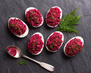 Stuffed eggs with beetroot with cream cheese, garlic and spicy herbs on a black slate background