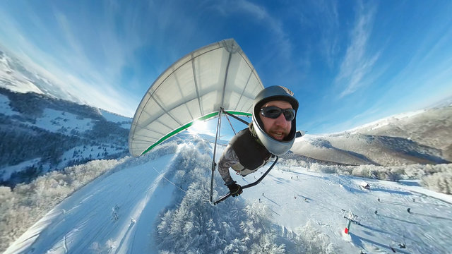 Funny smiling hang glider pilot fly fast above winter ski resort.