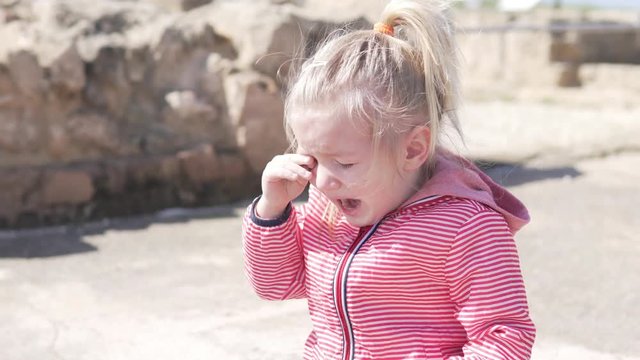 The little girl is crying. A child on the street in a jacket roars.