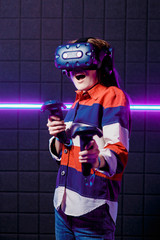 A young girl in a virtual reality helmet in the game room is playing a video game. 