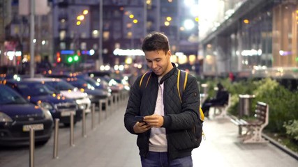 Young Attractive Man Using Smartphone in the evening city street with bokeh light effect.