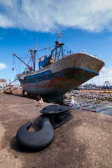 A fishing boat docked at the dock waits for a full repair with a boat hook in the foreground.