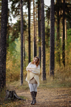 red-haired girl in bright clothes against a background of tree trunks in the autumn forest