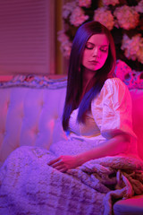 a beautiful girl in the light of a multi-colored light, on a chair with a soft rug, a gentle atmosphere in red-purple tones.