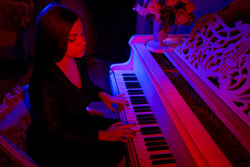 Beautiful girl and grand piano under the light of multi-colored lamps. Fantastic atmosphere of unusual colors. pianist girl playing a musical instrument piano in a dark room