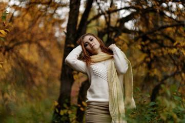 red-haired girl in bright clothes against a background of tree trunks in the autumn forest