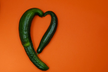 Ugly organic cucumbers shaped in a form of heart on orange background. Image with copy space, top view