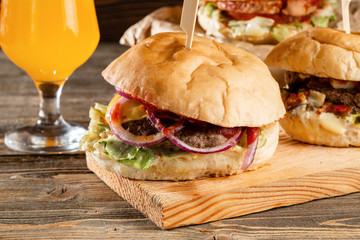Three big burger with meat cooked on BBQ coal. Lunch with Glass of juice on a wooden background. The concept of fast food and unhealthy food