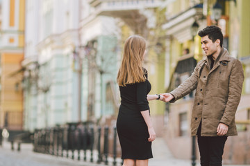 Urban modern young love couple walking romantic talking talking, holding hands on a date. Young multicultural Turkish brunette and Caucasian couple on old european street. Autumn spring weather