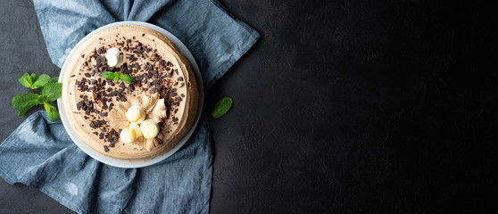 Tasty cake decorated with cream and dark chocolate on black background. Top view with copy space.