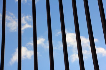 Fototapeta premium Silhouette of vertical bars of metal grating against the blue sky with clouds - geometric lines texture for environmental background