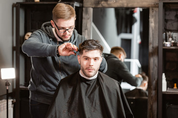 Barber work with clipper machine in barbershop. Professional trimmer tool cuts beard and hair on young guy in barber shop salon.