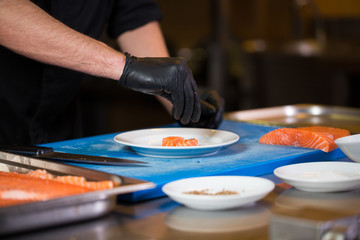Theme cooking is a profession of cooking. Close-up of a Caucasian man's hand in a restaurant kitchen preparing red fish fillets salmon meat in black latex gloves uniform