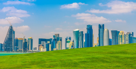 The Capital city of Qatar and Doha Bay from West Mound-Skyline viewpoint. Doha, Persian Gulf, Middle East, Arabian Peninsula. Sunny day. Urban scenary. Copy space with green lawn.