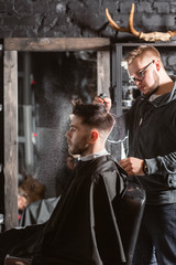 Barber sprays clean water on head in barbershop. Professional trimmer tool cuts beard and hair on young guy in barber shop salon.