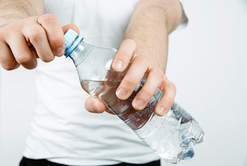 Drinking water from the bottle. A thirsty man is holding a bottle of water in his hand. The concept of thirst, the desire to drink clean water. Taking care of health, proper hydration of the body.