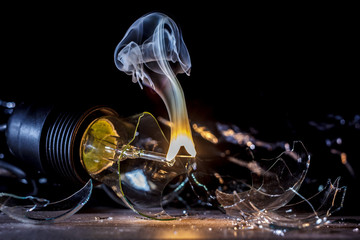 Amazing explosion of burning light bulb with splinters of broken glass and smoke on isolate black background. Сoncept of creative art illustrations of tungsten filament combustion in contact with air