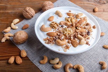 White plate with greek yogurt granola, almond, cashew, walnuts  on brown wooden background.
