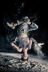 cool dirty japanese guy dancer in style bboying doing complex tricks on floor in Studio filled with flour on black background. concept of space dance on surface of planet moon. toned sepia, instagram