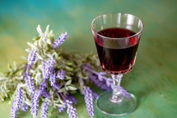 A glass of red wine and a bouquet of lavender flowers on a green table. Art photography. Closeup. Soft focus. Toned image doesn’t in focus.