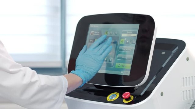 Doctor-cosmetologist setting up parameters of laser machine.