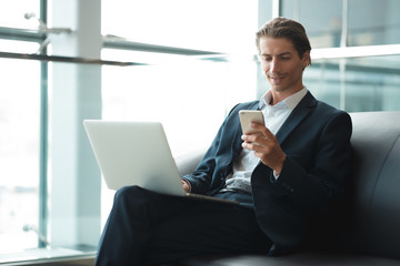 Young handsome man sitting in office with cup of coffee and working on project connected with modern cyber technologies. Businessman with notebook trying to keep deadline in digital marketing sphere.