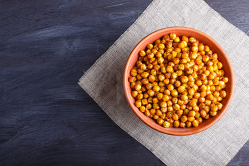 Fried chickpeas with spices in a clay plate on black wooden background.