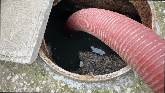 Pumping waste from concrete household septic tank of private house through large hose and open manhole