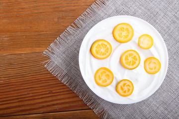 greek yogurt with kumquat pieces in a white plate on a brown wooden background