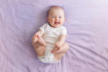Portrait of cute adorable smiling laughing white Caucasian baby girl boy with blue eyes four months old lying on bed looking at camera. View from top above. Happy childhood lifestyle. - 261865802
