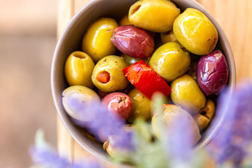 Olives stuffed with red pepper and herbs spices. Multi-colored olives in a bowl on a wooden table. Lavender. Blurry background. Close up. Soft focus. Top view.