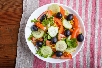 Vegetarian salad of tomatoes, cucumbers, parsley, olives and mustard on linen tablecloth.