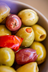 Olives stuffed with red pepper and spices of herbs. Multi-colored olives in a gray bowl. Blurry background. Macro. Image doesn’t in focus. Top view.