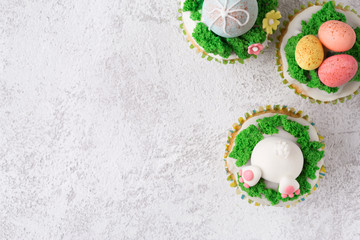 Festive cupcakes with funny bunny, eggs and grass on white background. Easter holiday concept. Top view with copy space