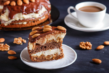 Homemade chocolate cake with milk cream, caramel and almonds on black wooden background. cup of coffee.
