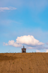 Fototapeta premium A small church sits alone on top of a hill with one puffy cloud above it